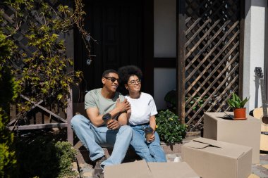 Kahveli Afro-Amerikan çift yeni evin verandasında karton kutuların yanında konuşuyorlar.