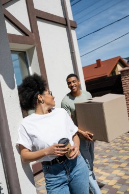 Gülümseyen Afro-Amerikan kadın elinde kahve paketli ve yeni eviyle erkek arkadaşının yanına gitmek için.