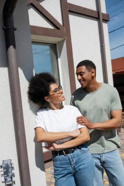 Gülümseyen Afrikalı Amerikalı bir adam yeni evin yakınında gözlüklü kız arkadaşına dokunuyor.