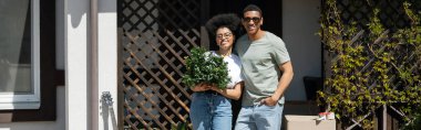 Positif Afro-Amerikan çifti karton kutu ve yeni evin yanında ev bitkisi tutuyorlar.