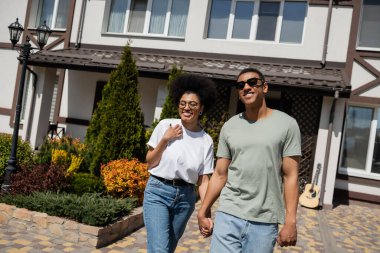 Olumlu romantik Afrikalı Amerikalı çift yeni evin yanında dururken el ele tutuşuyorlar.