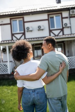Gülümseyen Afrikalı Amerikalı bir adam kız arkadaşına sarılıyor ve yeni bulanık evin yakınında konuşuyor.