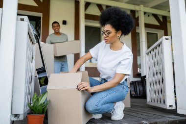 Afrikalı Amerikalı kadın, bulanık erkek arkadaşının ve yeni evinin yakınındaki karton kutuları açıyor.