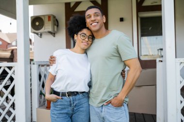 Arkaplanda bulanık yeni evin yakınında sarılıp poz veren Afro-Amerikan çift