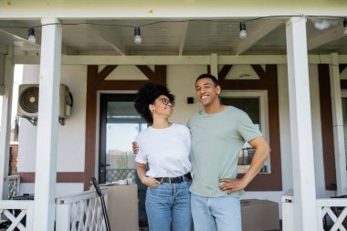 Gülümseyen Afrikalı Amerikalı çift yeni evin verandasında dururken sarılıyorlar.