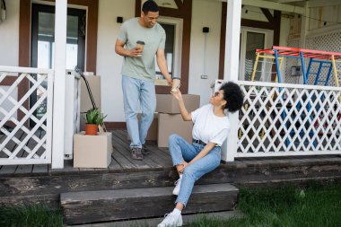 Pozitif Afro-Amerikalı adam yeni ev ve kutuların yanındaki kız arkadaşına kahve ikram ediyor.