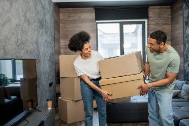 Pozitif Afro-Amerikan çift ellerinde karton kutular ve yeni evde oturma odasında gülümsüyor.