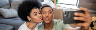 Afro-Amerikan çifti akıllı telefondan selfie çekiyor ve yeni evde dudak büküyor.