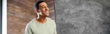 happy and smiling african american man looking away while standing in new house, banner clipart