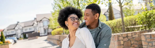 stock image positive african american couple looking at each other on urban street in summer, banner