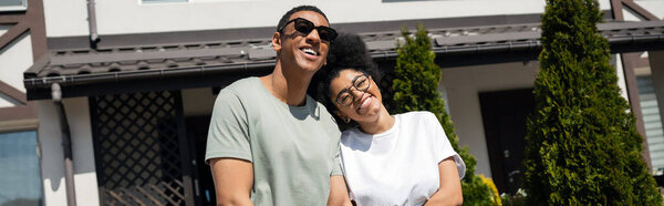 smiling african american couple standing near new house on background outdoors, banner