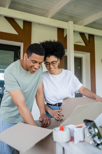 smiling african american couple unpacking cardboard boxes near new house outdoors