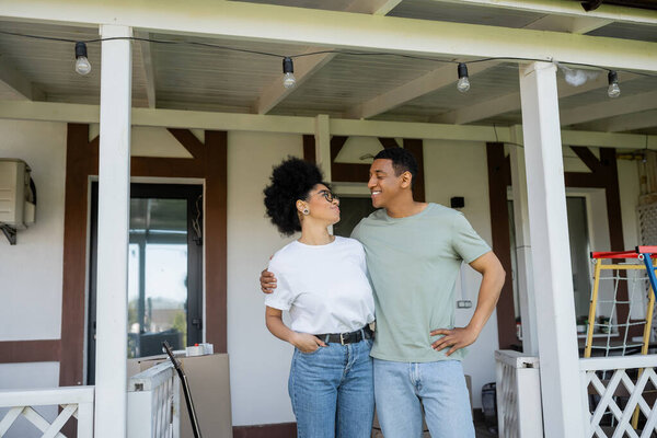 happy african american couple embracing while standing on porch near new house outdoors