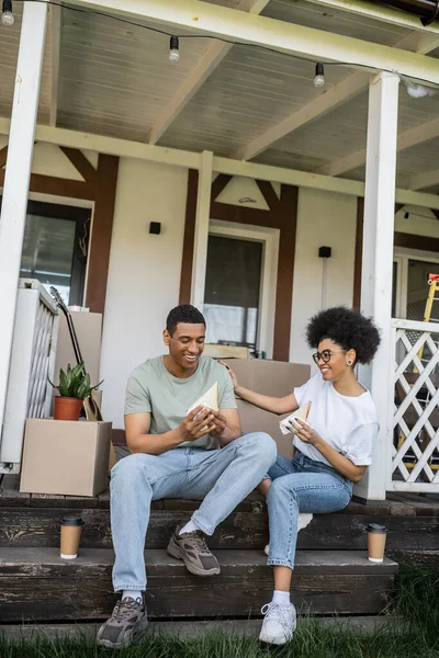 stock image positive african american couple with sandwiches and coffee talking on porch of new house