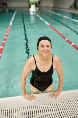Havuz başında yüzme şapkası ve gözlüklü neşeli orta yaşlı kadın, gülümsüyor, dinlenme merkezi, spa