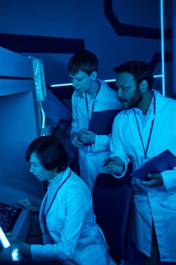 Exploring Tomorrow: Three Scientists Collaborate Near Futuristic Computer in Science Center clipart
