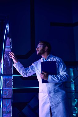 Gelecekteki bilim, gözlüklü Hintli bilim adamı neon ışıklı yenilik merkezindeki yeni ekipmanları inceliyor.