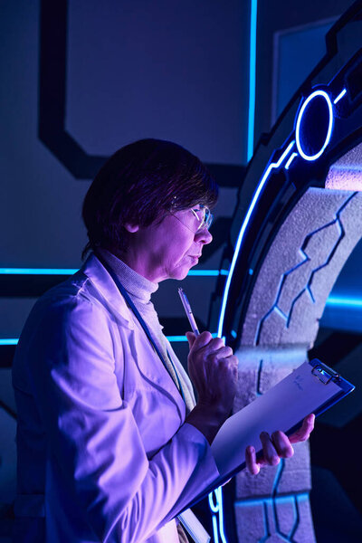 futuristic science, middle aged woman scientist thinking near innovative device in discovery center