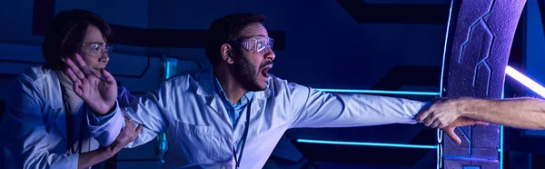 stock image scared multiethnic scientists near hand in experimental device in discovery center, banner