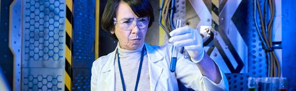 middle aged woman scientist in goggles looking at liquid in test tube in innovation lab, banner