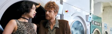 Çamaşırhanedeki çamaşır makinesinin yanında Asyalı kız arkadaşına bakan modacı genç adam.