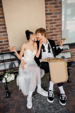 Avrupa 'da bankta oturmuş pizza yiyen ırklar arası yeni evliler açık havada kutlama yapıyorlar.