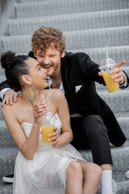 Neşeli kızıl damat, parmaklarıyla caddede portakal suyu ile Afro-Amerikan gelinini işaret ediyor.
