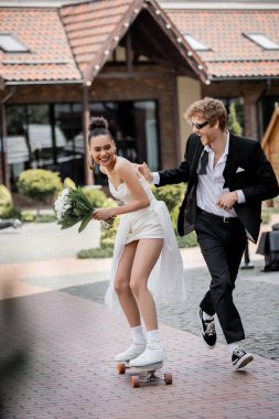 Güneş gözlüklü neşeli damat, Afrika asıllı Amerikalı gelinin elini tutuyor.