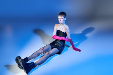 Mavi arka planda oturan korseli ve botlu bir model pembe eldivenli, tuhaf bir moda.
