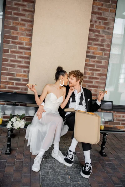 优雅的多种族夫妇 在长椅上亲吻比萨饼 在城市举行婚礼 在户外庆祝 — 图库照片