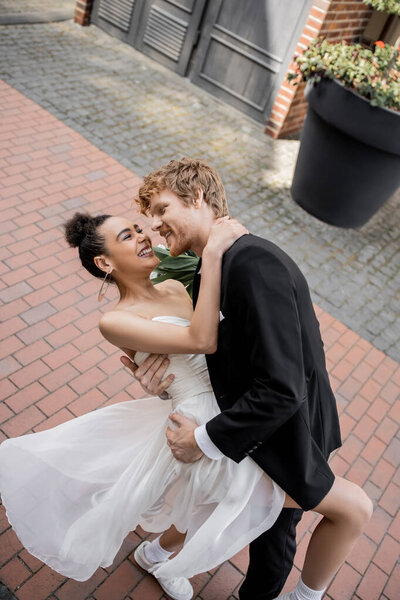 high angle view of stylish interracial newlyweds embracing on street, unusual wedding in city