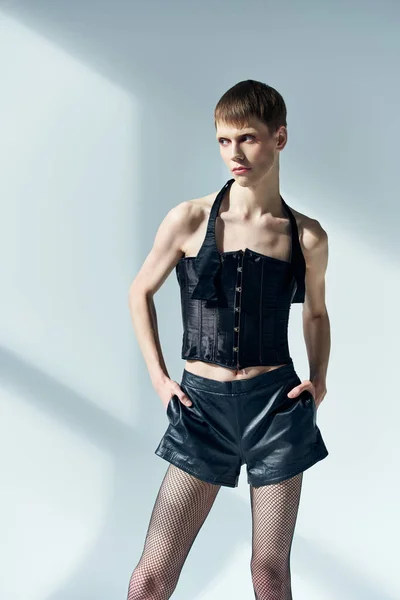 stock image androgynous model in black corset and shorts posing on grey, lgbt, queer fashion, hands in pockets