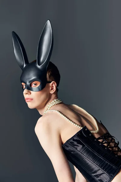 queer person in black corset and bdsm bunny mask posing on grey, corset lacing, edgy fashion