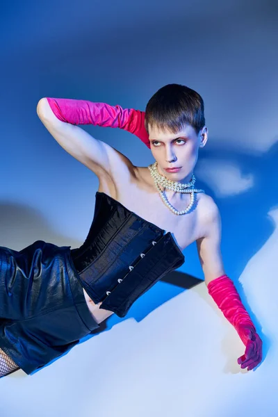 stock image queer person in bold outfit and pink gloves posing on blue backdrop, nonbinary model, fashion