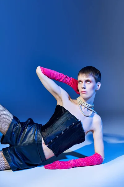 queer person in bold outfit and pink gloves posing on blue backdrop, shorts, nonbinary model, style