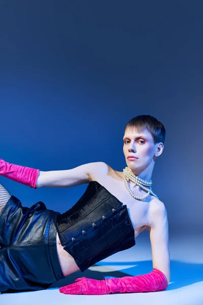 stock image queer model in bold outfit and pink gloves posing on blue backdrop, shorts, nonbinary, style