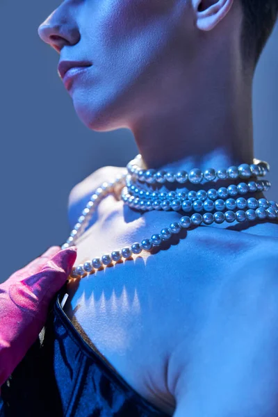 stock image close up and details, genderfluid model with pearl necklace posing in pink glove on blue backdrop