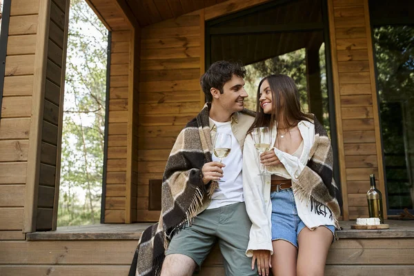 バックグラウンドでチーズやバケーションハウスの近くでワインを保持する毛布で微笑むカップル — ストック写真