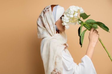 Başörtüsü ve bluzu olan, bej renkli beyaz çiçekli mütevazı Müslüman kadının yan görünüşü.