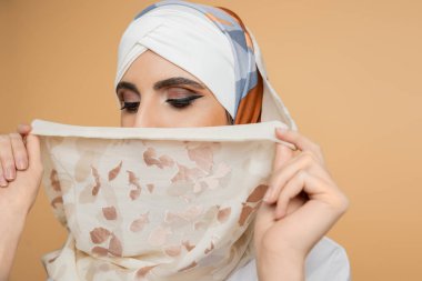 Makyajlı, mütevazı Müslüman kadın bej üzerine ipek başörtüsü takmış, yüzü kararmış.