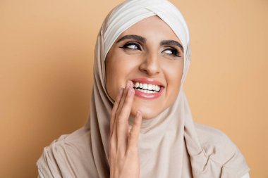 Çekici, neşeli, makyajlı, tesettürlü, gülen ve bej rengi gözleriyle yüzünü çeviren Müslüman kadın.