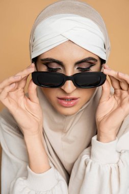 tesettürlü çekici Müslüman kadın bej, kişisel stil, bireysellik üzerine moda güneş gözlüğünü çıkarıyor.