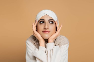 Olumlu ve rüya gibi Müslüman bir kadının portresi tesettürlü, elleri bej rengi yüzün yanında başka tarafa bakıyor.