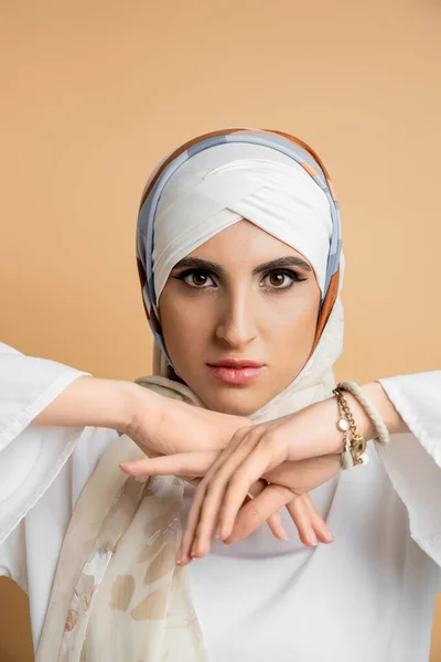 stock image charming middle eastern woman in elegant silk scarf looking at camera on beige, muslim beauty