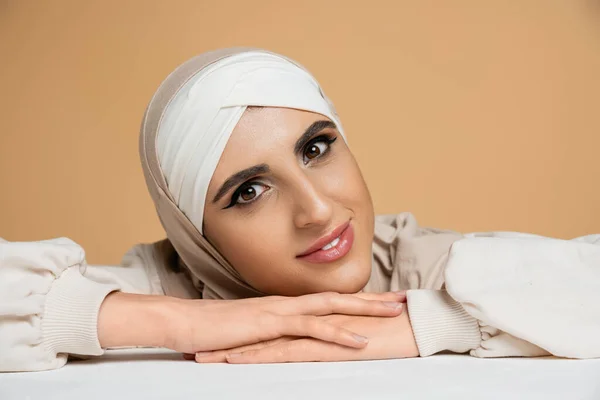 portrait of middle eastern woman in hijab, with makeup looking at camera on beige, muslim beauty