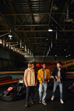 Neşeli çeşitli arkadaşlar sohbet ediyor ve yarış arabalarının yanında yürüyor Karting pistinde, motorsporda