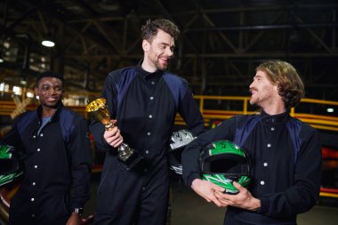 Heyecanlı adam altın kupa tutuyor ve Go-kart yarışının galibi olarak çeşitli sürücülere yaklaşıyor.