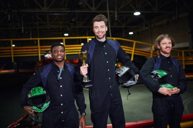 Altın kupa tutan mutlu sürücü ve Go-kart yarışının galibi olarak çeşitli rakiplerin yanında duruyor.
