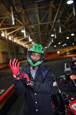 Eldiven takan ve go-kart 'ın yanında duran hırslı Afro-Amerikan motorlu sürücü.