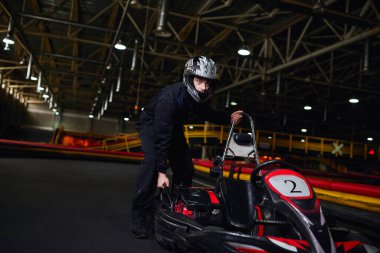Motor sporu ve hız sürücüsü, spor kıyafetlerinde odaklanmış kart sürücüsü ve pistte go kart itme kask